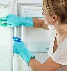 Žena v rukavicích čistí chladničky s pomocí čisticího prostředku.